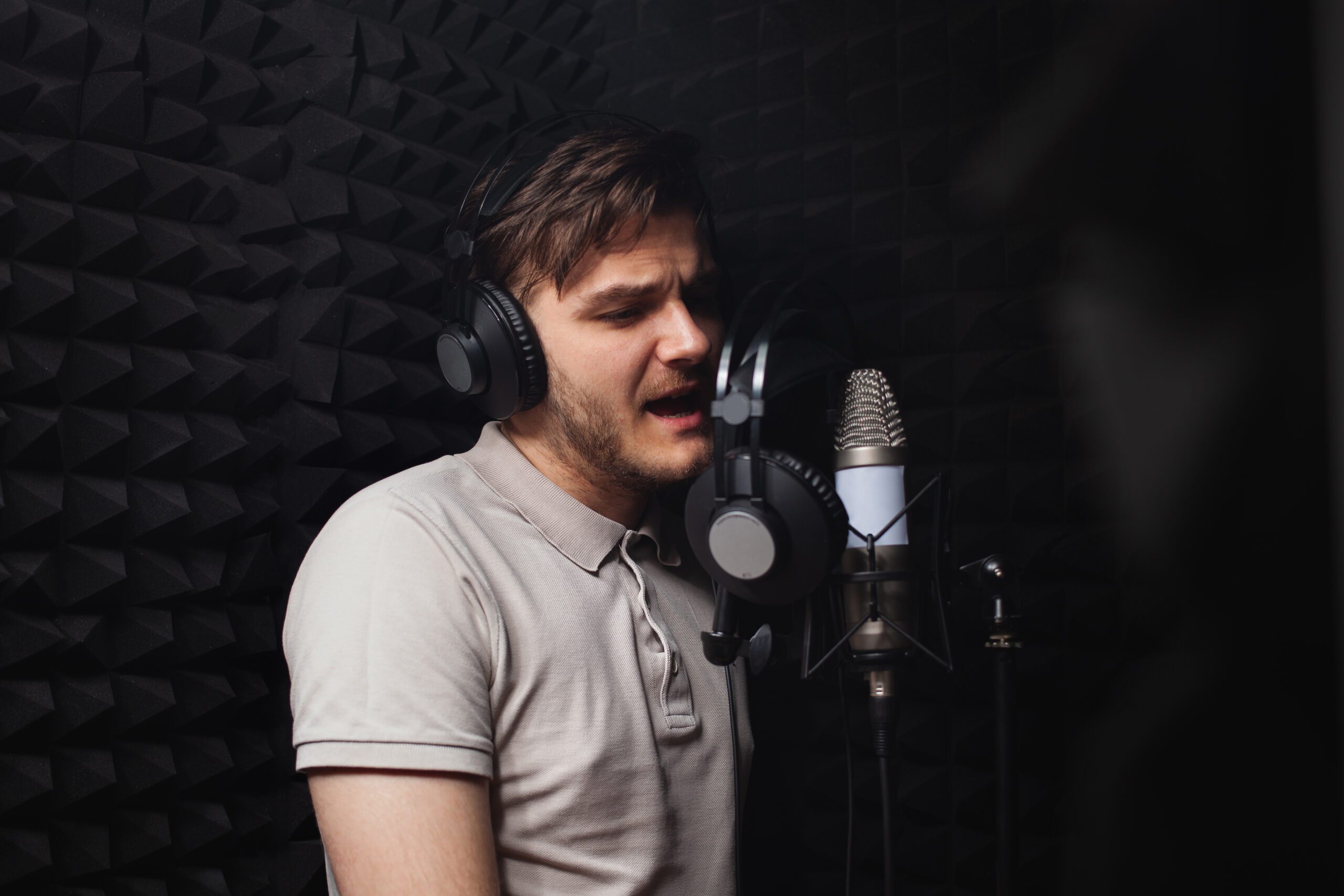man sings into microphone, professional recording studio, headphones. Black soft walls, sound insulation. singer records his song.
